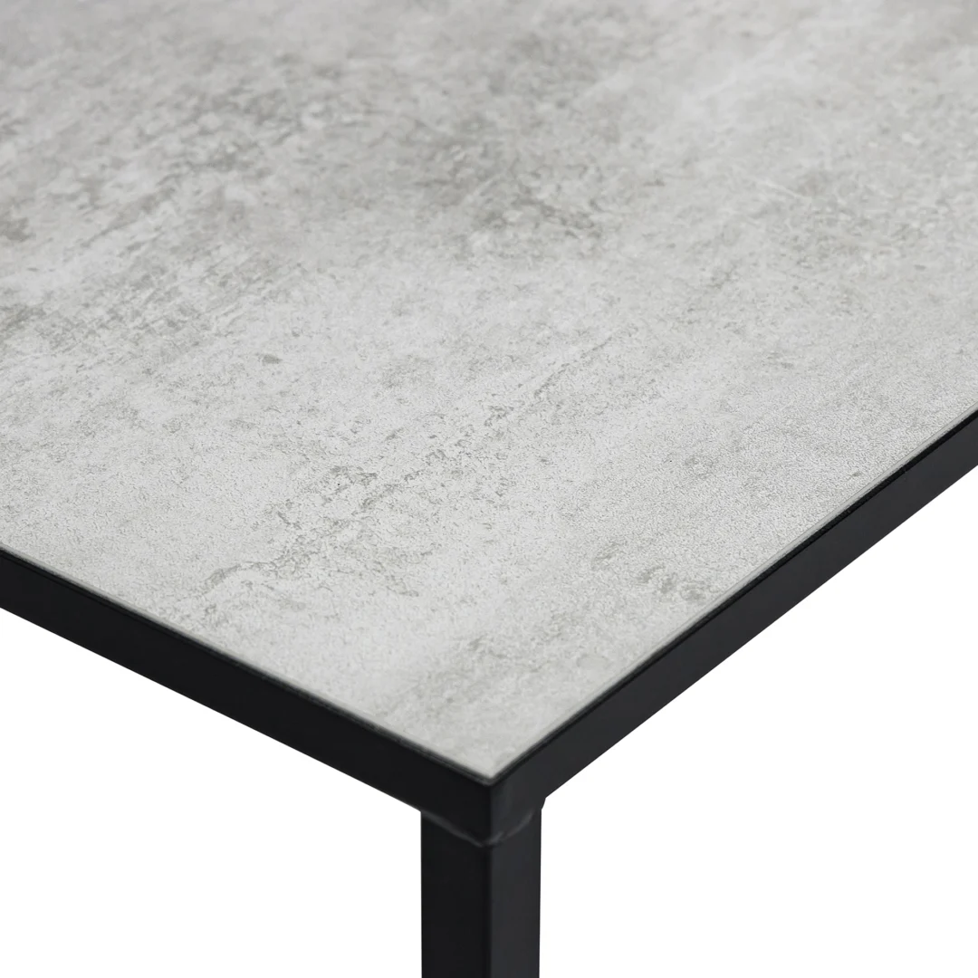 Een close-up van Salontafel Zwart 67 x 44 CM Beton toont de rechthoekige vorm, het lichtgrijze tafelblad dat lijkt op beton en het stevige zwart metalen frame, met de nadruk op de hoek en een deel van het oppervlak.