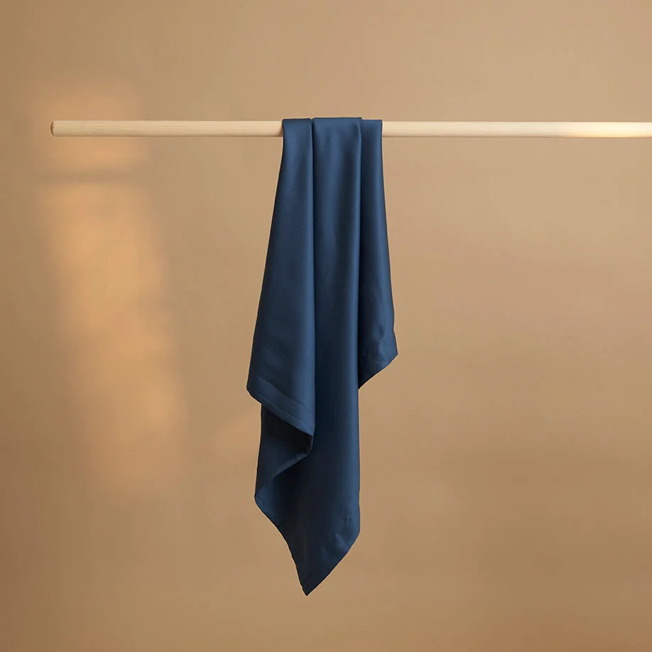 Blauwe kussensloop van TENCEL Lyocell, hangend aan een houten stang. Zachte stof met subtiele glans, tegen een beige achtergrond.