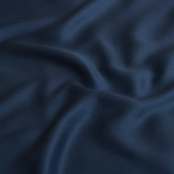 Close-up van een blauwe kussensloop van TENCEL Lyocell. De stof is zacht en golvend, met subtiele lichtreflecties. Ideaal voor een rustige slaap.