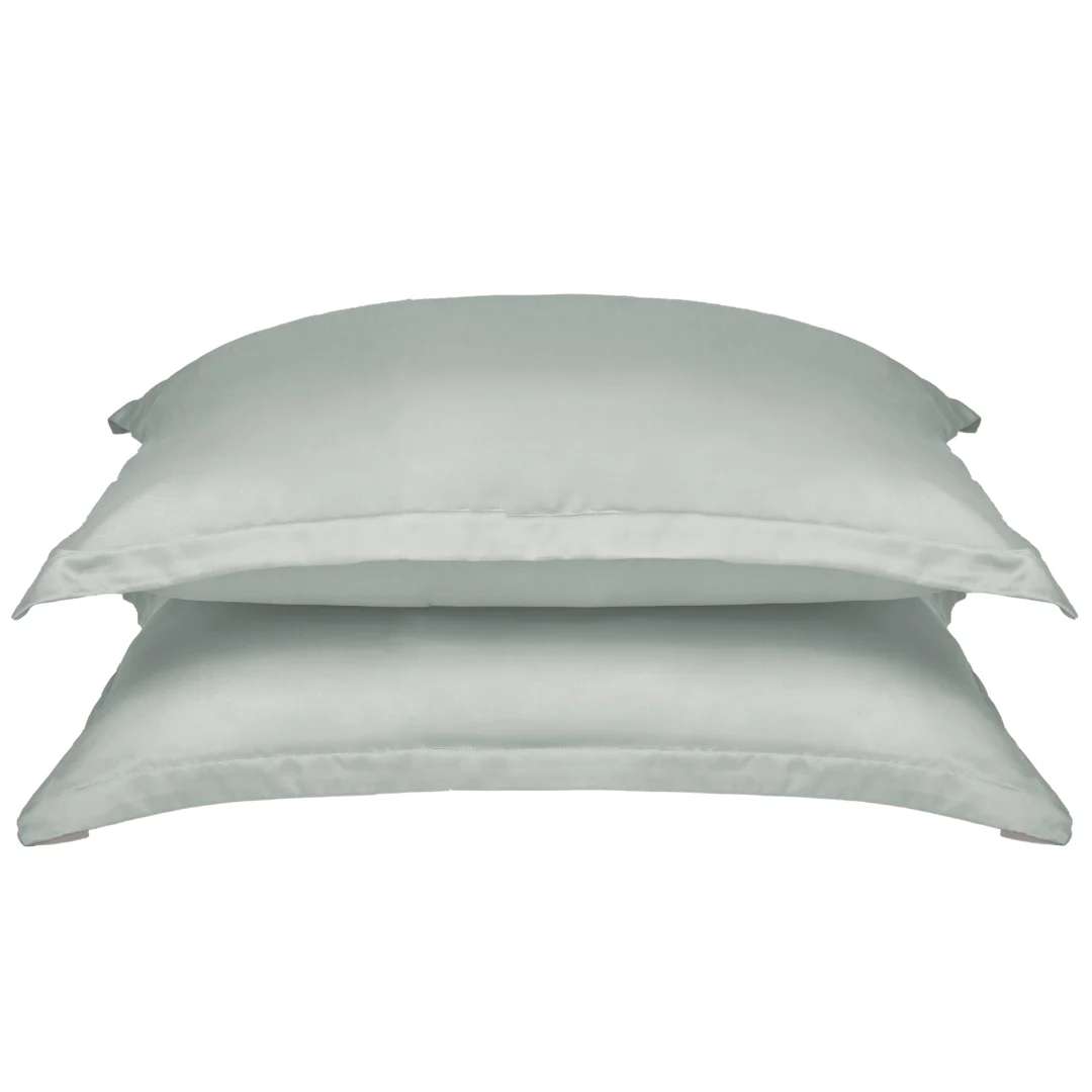 Twee gestapelde, lichtgrijze kussenslopen van Tencel lyocell op een witte achtergrond. Zachte belichting, effen stof zonder patroon.