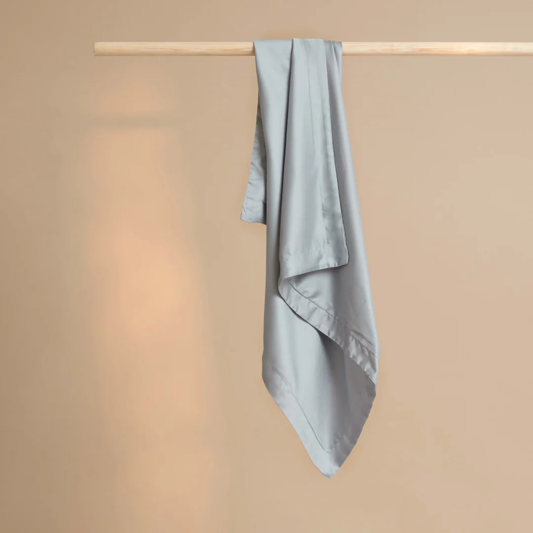 Een Kussensloop 60x70 Grijs Comfortabele touch drapeert soepel over een houten roede, tegen een eenvoudige beige achtergrond.