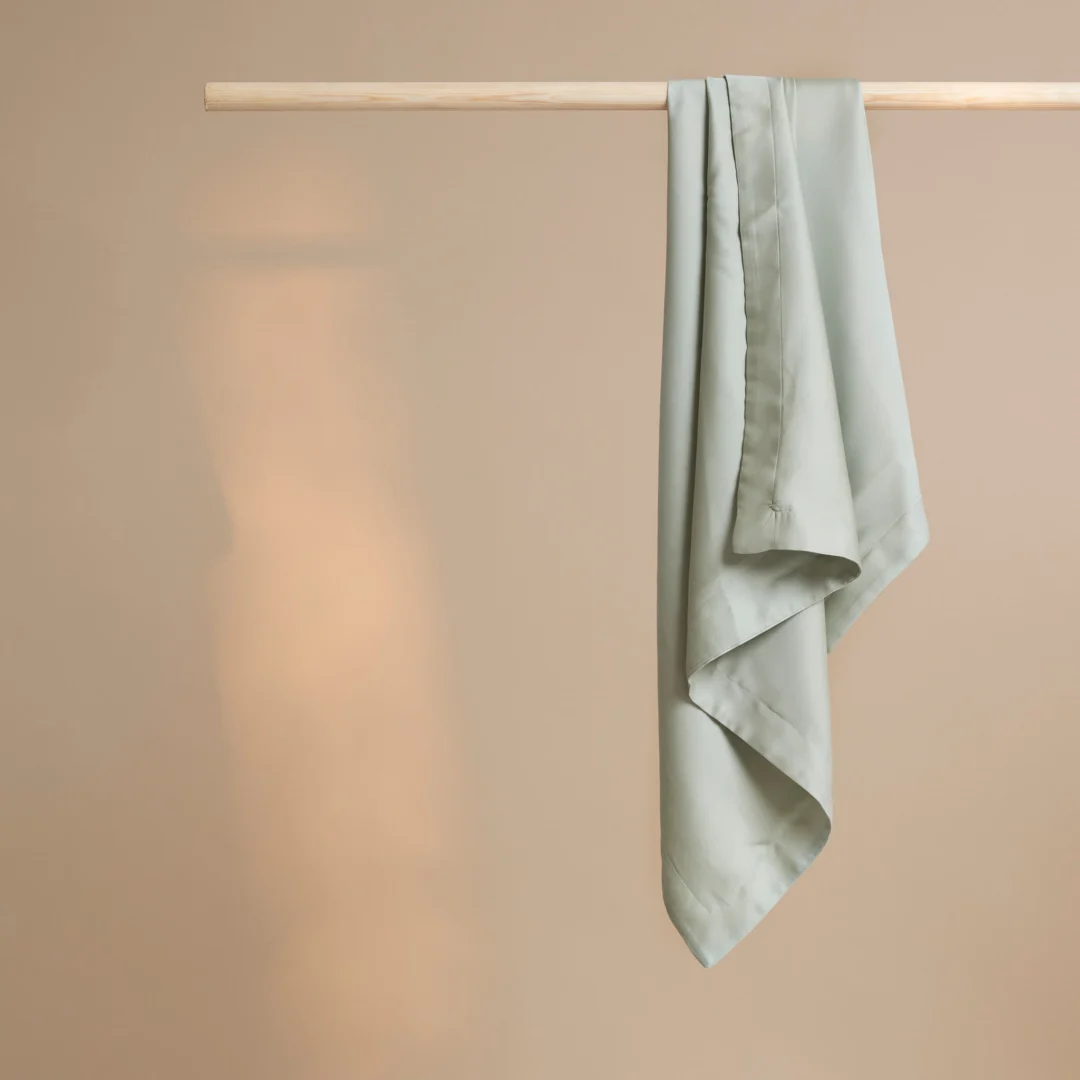 De Dekbedovertrek 60x70 Grijs Comfortabele is netjes gedrapeerd over een houten roede, tegen een effen beige achtergrond.