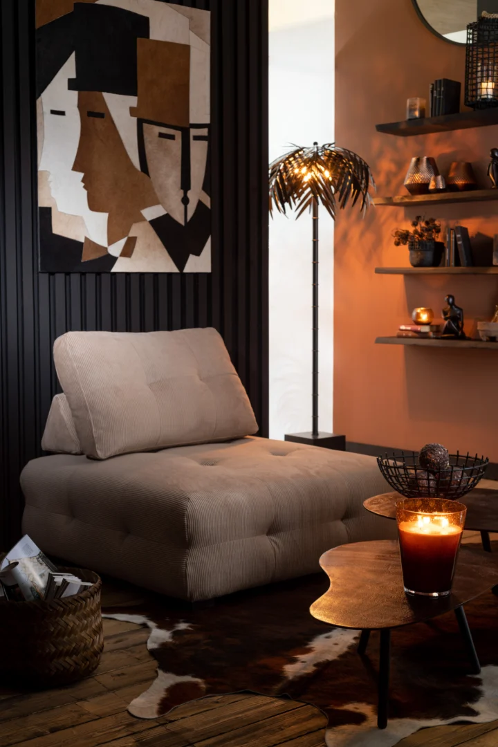 Een gezellige loungehoek met een beige stoel met kussens, een tapijt van koeienhuid, een modern abstract schilderij, een vloerlamp in de vorm van een palm, zwevende planken met decor en een brandende kaars op Salontafel Zwart 32 CM Aluminium.