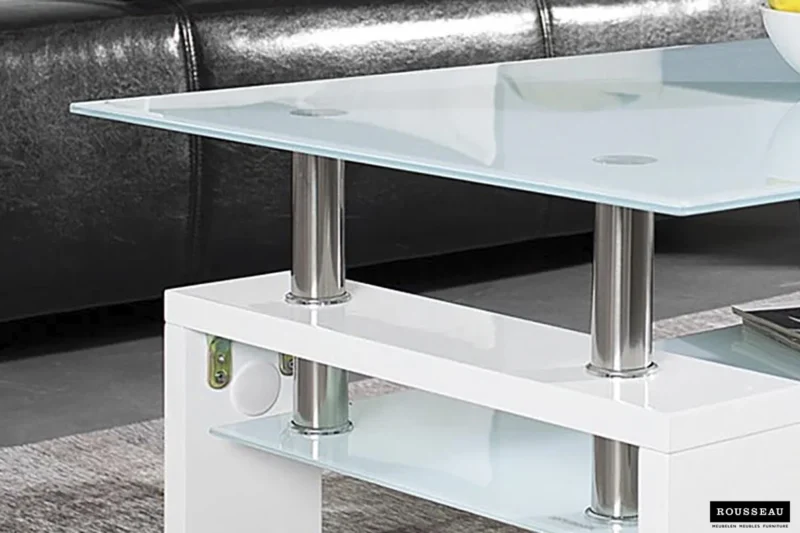 De Salontafel Wit Design Modern, een strakke glazen salontafel met metalen steunen en een glanzend wit onderstel, staat op een grijs vloerkleed voor een zwart leren bank. Het logo van het merk Rousseau staat rechtsonder.
