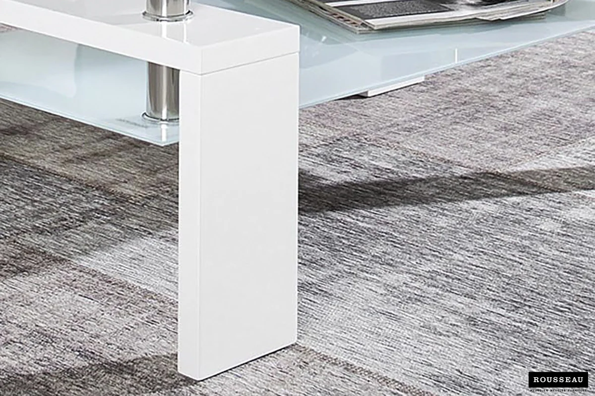 Close-up van de Salontafel Wit Design Modern, een strakke witte salontafel met een glazen plank eronder, geplaatst op een grijs gestructureerd tapijt. Een tijdschrift is gedeeltelijk zichtbaar op de glazen plank.