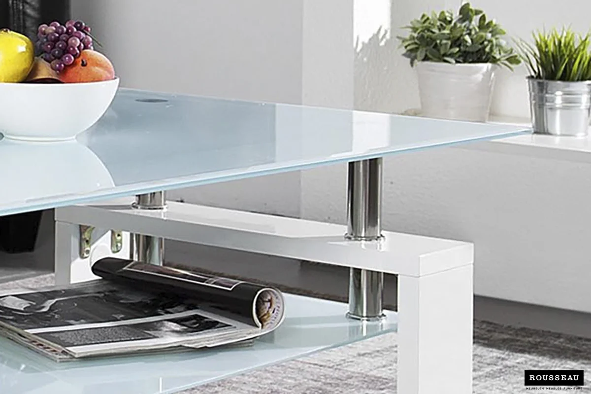 De Salontafel Wit Design Modern is een moderne glazen salontafel met een fruitschaal bovenop en een opgerold tijdschrift op de onderste plank, verlicht door zonlicht dat door een raam naar binnen schijnt.