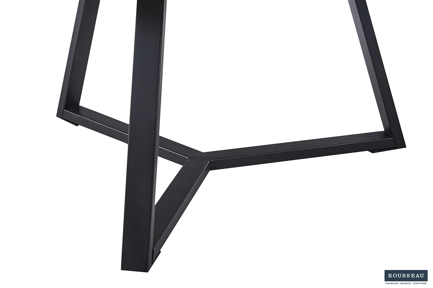 De Salontafel Design Tijdloos heeft zwart metalen poten die een geometrische driehoekige basis vormen, gezien vanuit een lage hoek tegen een witte achtergrond. Het Rousseau logo is zichtbaar in de rechter benedenhoek.