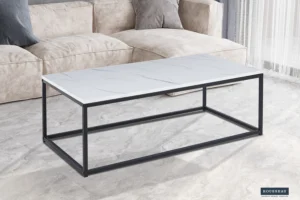 De Salontafel Wit Marmer Design, met een modern rechthoekig blad in wit marmerlook en een zwart metalen onderstel, staat op een lichtgrijze marmeren vloer voor een beige bank met grijze en beige kussens.