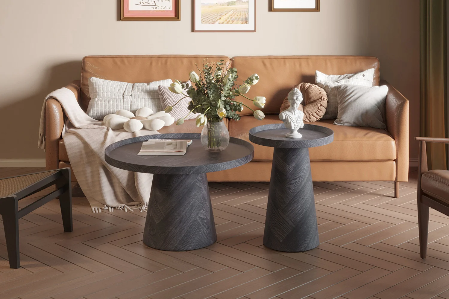 Een moderne woonkamer met een bruine leren bank, neutrale kussens, een beige kleed, twee Salontafel Donkergrijs, Roest 80 CM salontafels, een bloemenvaas, een kleine witte buste, ingelijste kunst aan de muur en visgraat houten vloeren.