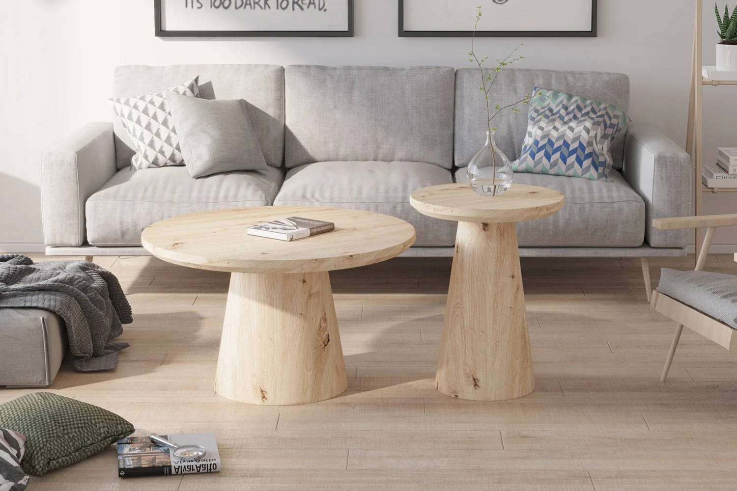 Een moderne woonkamer heeft een lichtgrijze bank, geometrische kussens, de Salontafel 80 CM Rond salontafel, een glazen vaas met een enkele tak, ingelijste kunst boven de bank en veel natuurlijk licht.