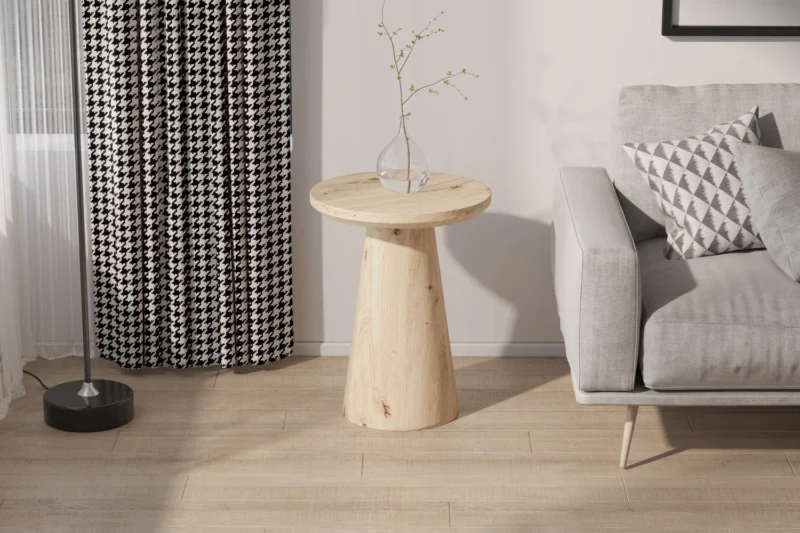 De Salontafel 45 CM, een ronde houten bijzettafel, staat naast een grijze bank met een geometrisch kussen; vlakbij hangen zwart-wit gedessineerde gordijnen, een staande lamp en in de ruimte ligt een lichte houten vloer.