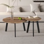 Twee salontafels met zwarte poten van Salontafel Roest Mangohout Design staan op een licht tapijt voor een beige bank. Op de ene staan twee groene appels en een glazen vaas met bladsteel; op de andere ligt een open boek. Ontwerp Tijdloos.