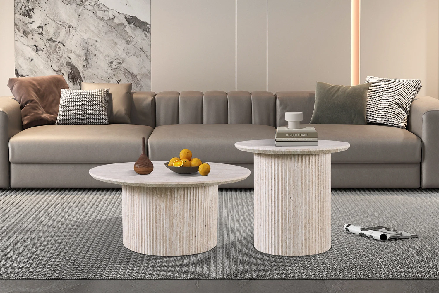 Moderne woonkamer met een grijze bank, diverse kussens, twee Salontafel Beige 80 CM Rond Travertin salontafels, decoratieve objecten, een schaal citroenen en een grijs vloerkleed. Een tijdschrift ligt bij de tafels.