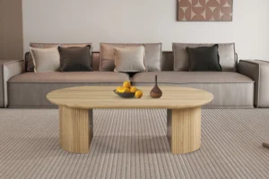 Een moderne woonkamer heeft een beige bank met neutrale kussens, een licht houten Salontafel 120 CM ovale salontafel met gebogen poten, met daarop een fruitschaal en een decoratieve vaas. Boven de bank hangt kunst met een patroon.