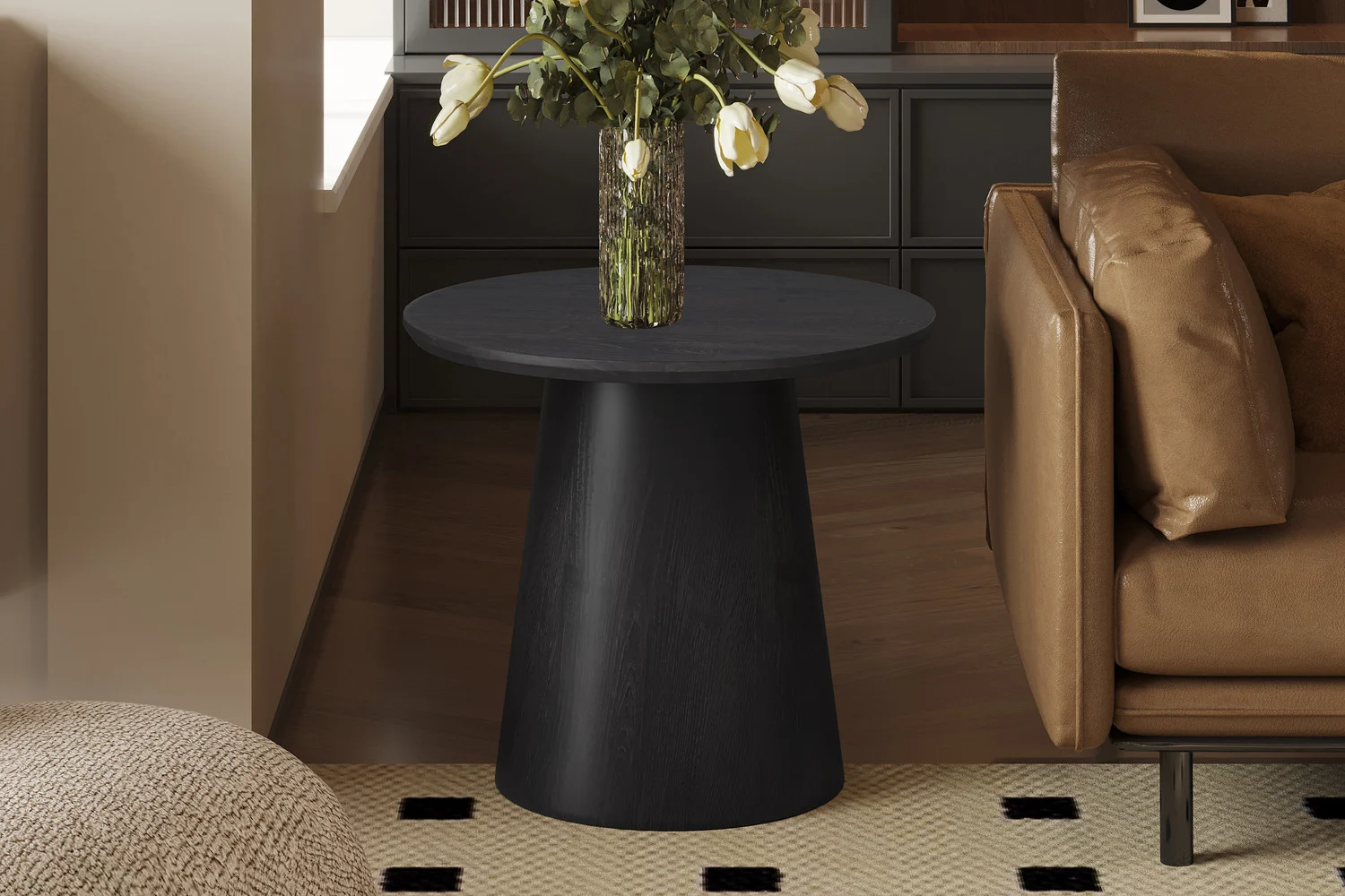 De 'Miklos' 60 cm ronde donkerbruine bijzettafel met een vaas bloemen staat naast een bruine leren bank in een moderne woonkamer met bruine tinten en een vloerkleed met patroon.