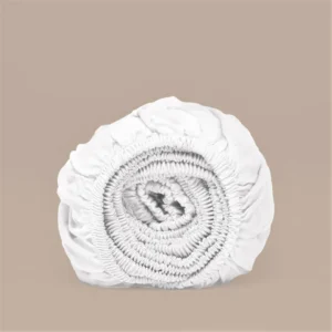 Opgerold wit hoeslaken. Zachte TENCEL™ Lyocell stof, elastische randen. Neutrale achtergrond, zacht licht. Duidelijke textuur van het materiaal.