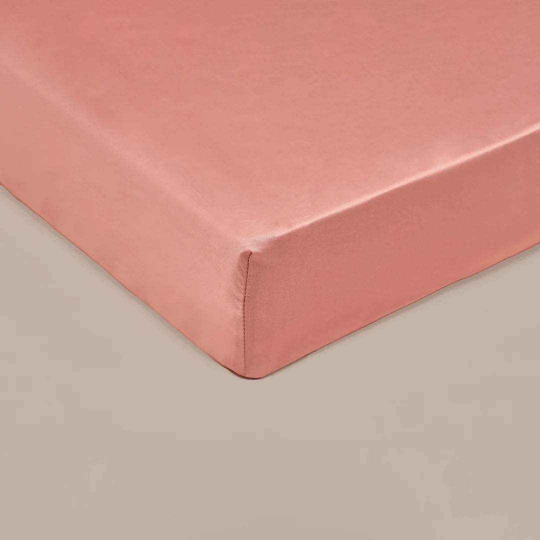 Detailopname van een terra roze topper hoeslaken. De stof is glad en strak getrokken, met zachte belichting en een neutrale achtergrond.
