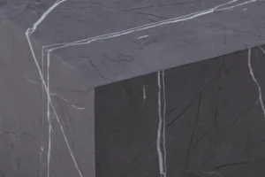 Een close-up van de Bijzettafel Grijs MDF Minimalistisch, met een donkergrijs oppervlak met prominente witte aderen over de bovenkant en zijkanten, die de scherpe hoeken en minimalistische, natuurlijke steenachtige textuur laten zien.
