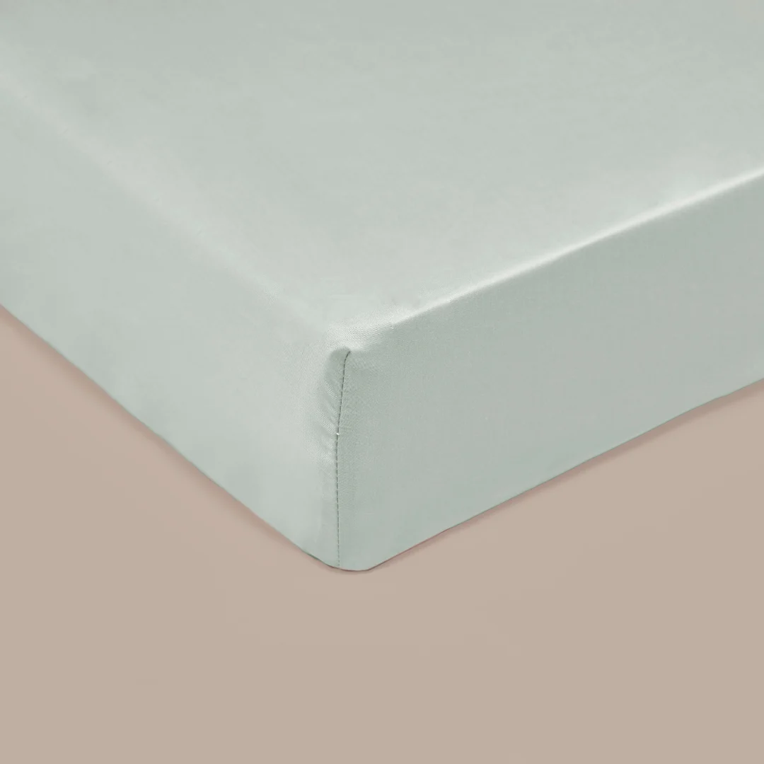 Close-up van een groen TENCEL™ hoeslaken op een matras, zachte belichting. De stof oogt glad en ademend, met een subtiele glans.