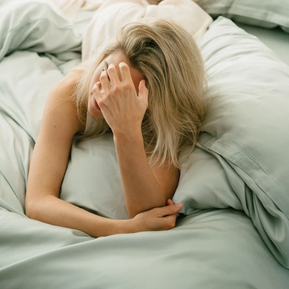 Vrouw ligt op groen TENCEL™ hoeslaken. Zachte belichting, lichte kleuren. Beddengoed oogt comfortabel en ademend. Close-up, bovenaanzicht.