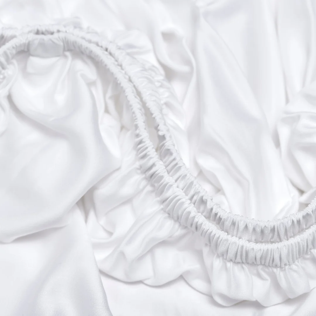 Detailopname van een wit TENCEL satijnen hoeslaken met elastiek. Zachte, glanzende stof in close-up, helder belicht.