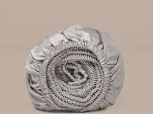 Oprolbaar taupe hoeslaken van satijn TENCEL™, zijdezacht. Zachte, neutrale achtergrond. Elastische randen zichtbaar in detail.