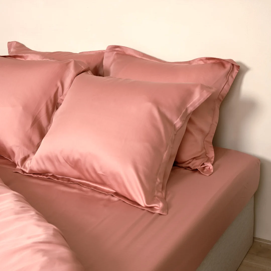 Close-up van een terra roze hoeslaken en kussenslopen van TENCEL™ satijn op een bed. Zachte, warme belichting.