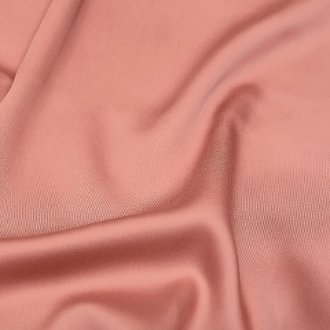 Close-up van een terra roze hoeslaken, TENCEL™ satijn. Zachte plooien vangen het licht, wat de luxe uitstraling benadrukt.