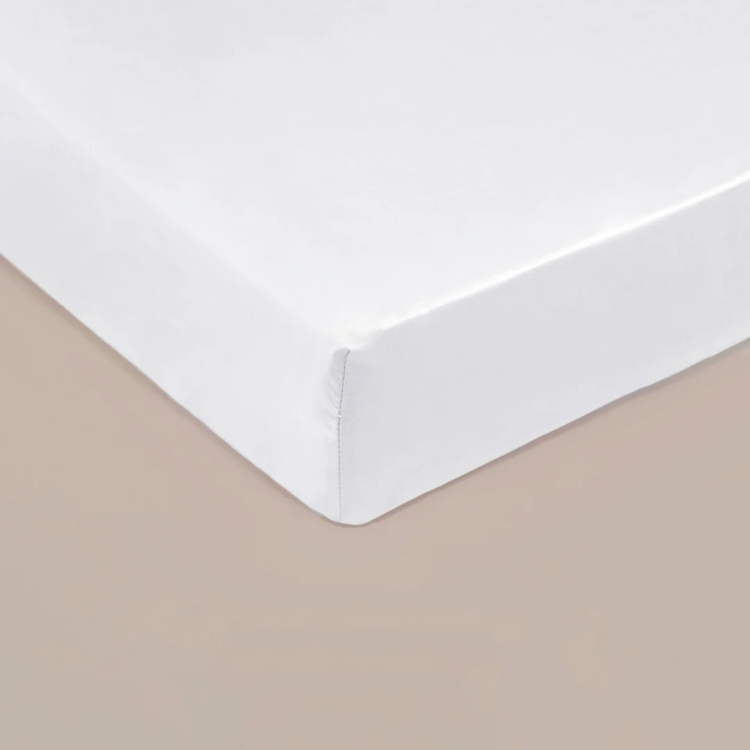 Close-up van een wit hoeslaken, strak getrokken over een matras. Zachte belichting, effen achtergrond. Hoogwaardig TENCEL™ Lyocell materiaal.