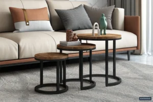 De Bijzettafel 'Plano' 3-delig Mango hout set - drie ronde houten nesttafels met zwart metalen frames - staat voor een beige en bruine bank met gedessineerde kussens, bekleed met decor en op een grijs gedessineerd vloerkleed.