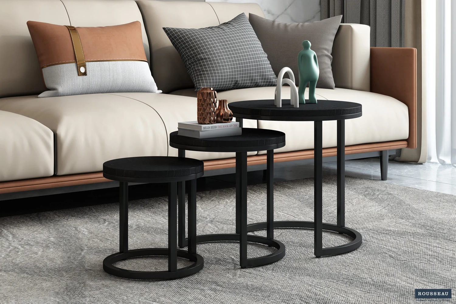 Drie moderne zwarte 'Plano' 3-delige mangohouten bijzettafels staan voor een beige bank met grijze en bruine kussens. Op de tafels staan decoratieve voorwerpen en eronder ligt een tapijt met een grijs patroon.