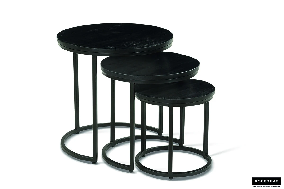 De bijzettafel 'Plano' 3-delig Mango hout zwart bestaat uit drie ronde zwarte nesttafels in verschillende maten met metalen poten, gerangschikt zodat de kleinere tafels gedeeltelijk onder de grotere schuiven. Het Rousseau logo staat rechtsonder.