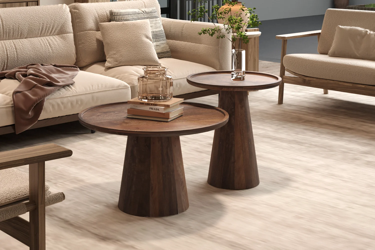 Een Salontafel 65 x 40 CM Rond Mangohout staat op een lichthouten vloer tussen beige banken met een glazen vaas met groene takken, terwijl een tweede ronde tafel vlakbij een glazen pot en een stapel boeken toont.