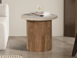 De Bijzettafel 'Louis' 50 cm, gemaakt van mangohout met een beige travertijnen blad, bevat een glas ijswater en een stapel tijdschriften, geplaatst naast een beige bank op een gepolijste vloer.