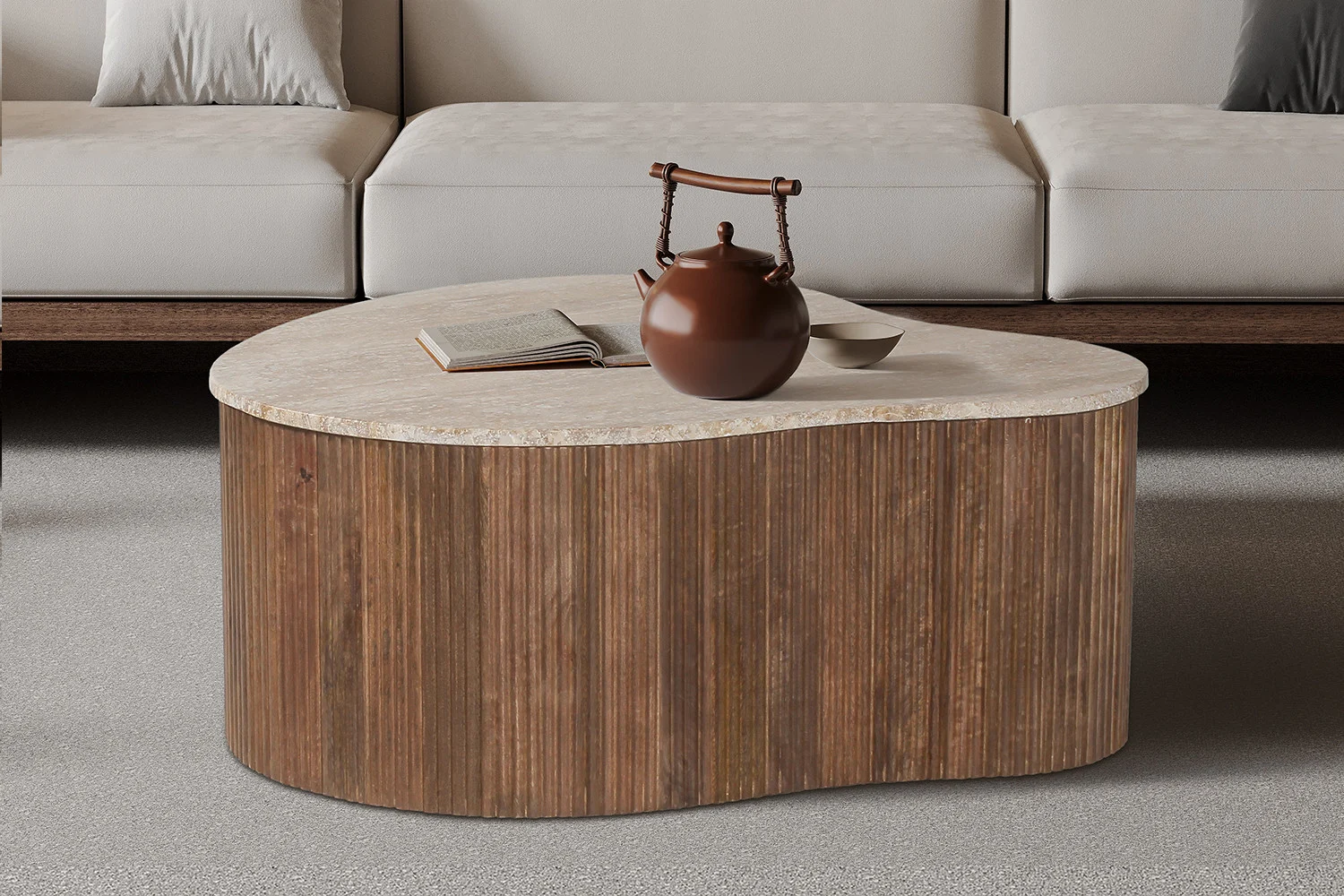 Een moderne woonkamer toont de Salontafel Beige 83 CM Travertin, een organisch gevormde salontafel met een licht stenen blad, naast een beige bank en versierd met een bruine keramische theepot, een kom en een open boek.