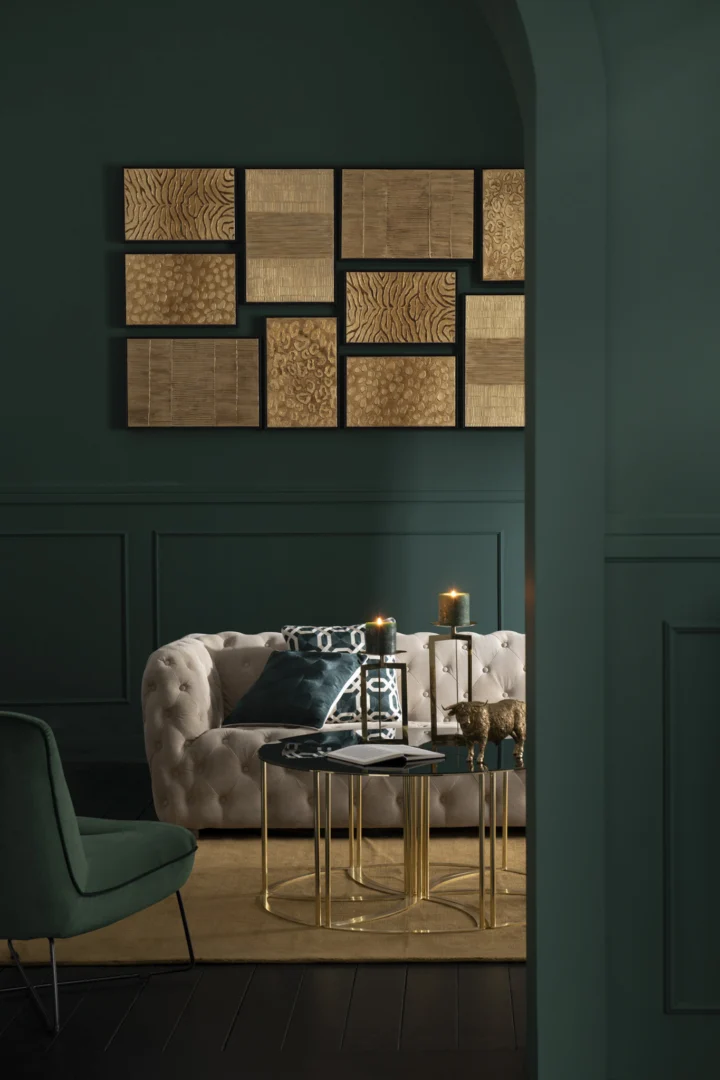 Een stijlvolle woonkamer met donkergroene muren, een getufte beige bank, een groene stoel, de Bijzettafel 100 x 48 CM Vierkant Metaal met kaarsen en geometrische gouden muurkunst boven de bank.