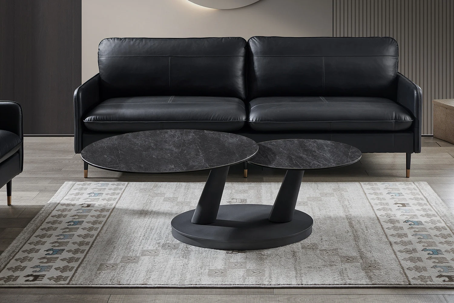 Een moderne woonkamer met een zwarte leren bank, twee Salontafel Donkergrijs, Roest Rond Steen salontafels en een vloerkleed met patroon op een lichte houten vloer.