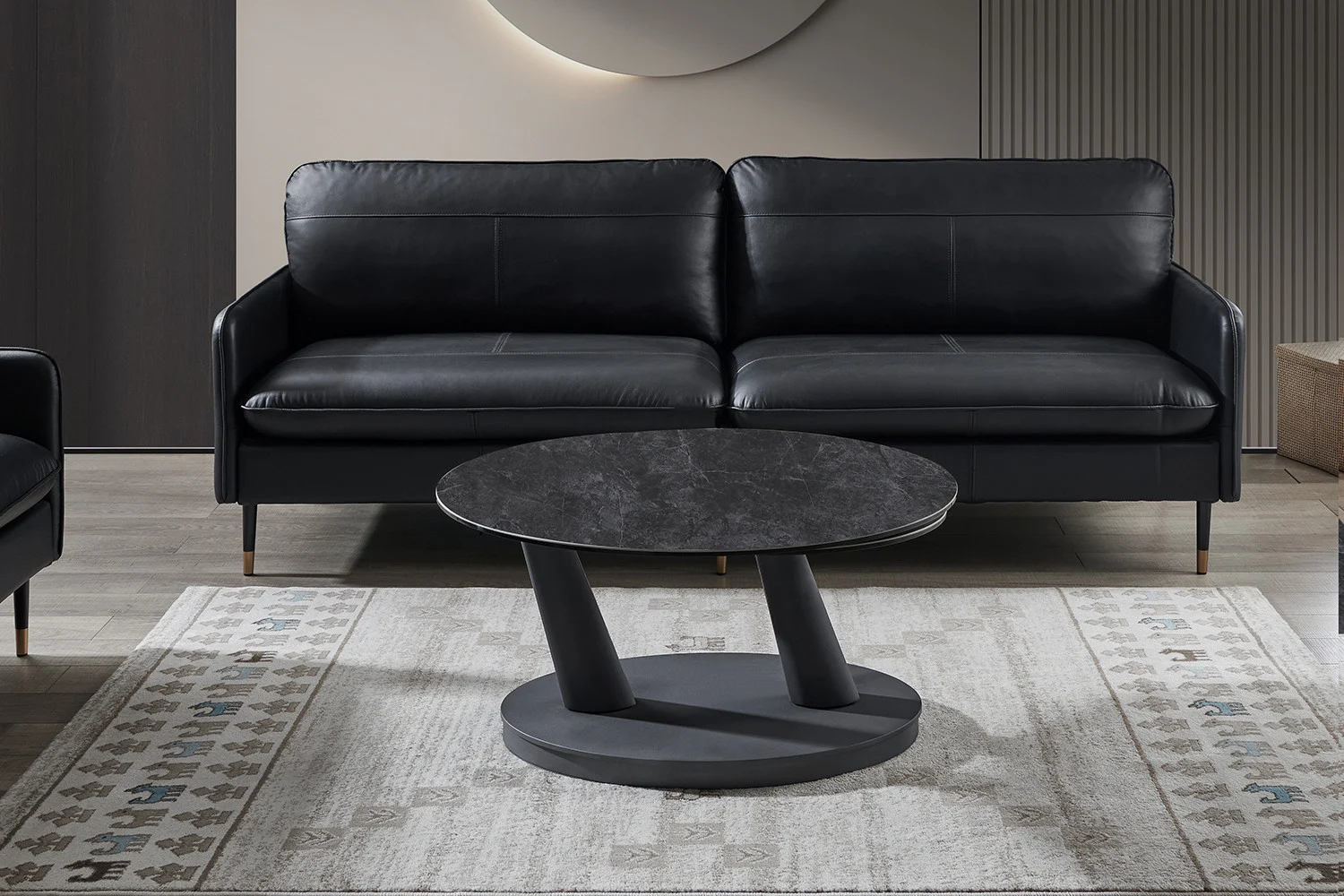 Een moderne zwartleren sofa staat achter de salontafel Donkergrijs, Roest Rond Steen, geplaatst op een gedessineerd vloerkleed in een hedendaagse woonkamer met neutrale tinten.