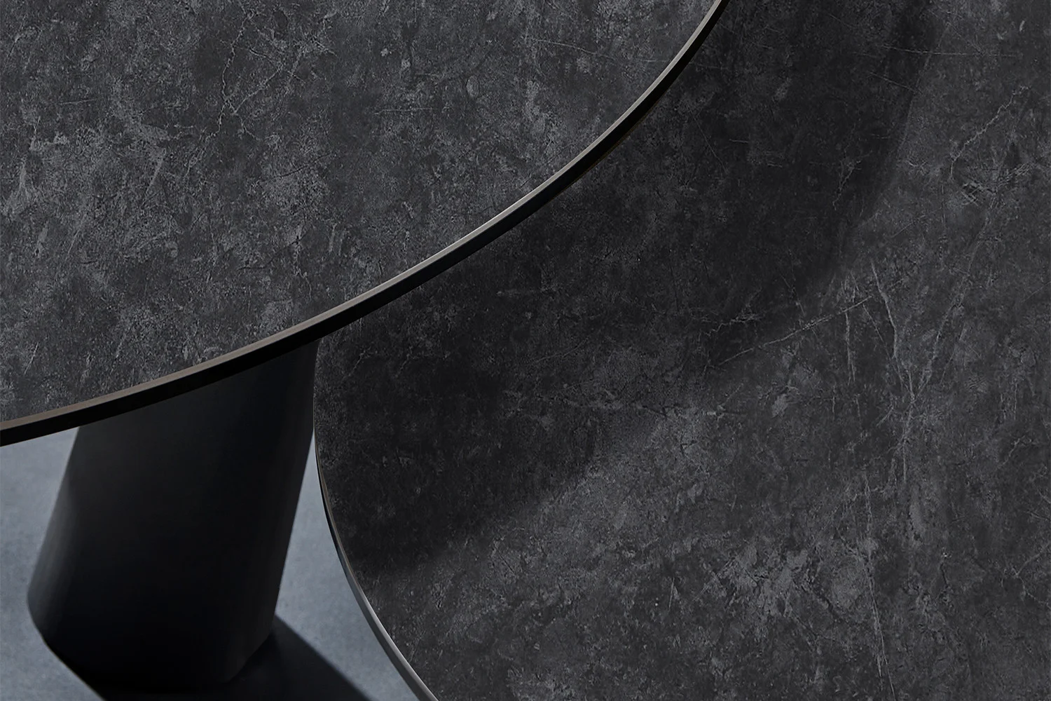 Een close-up van twee elkaar kruisende tafelbladen van Salontafel Donkergrijs, Roest Rond Steen met een gestructureerd oppervlak en een minimalistisch ontwerp.