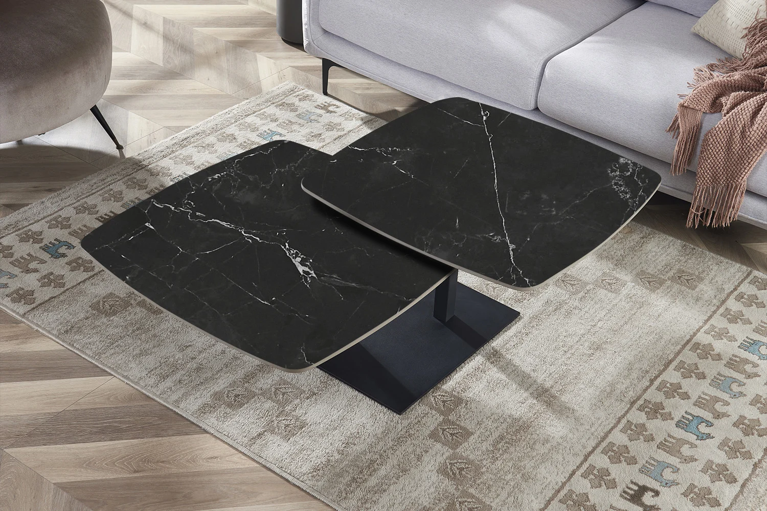 Een paar Salontafel Zwart Rond Steen salontafels met moderne zwarte stenen bladen en witte adering staan samen op een beige vloerkleed met patroon naast een lichtgrijze bank in een stijlvolle woonkamer met houten parketvloer.