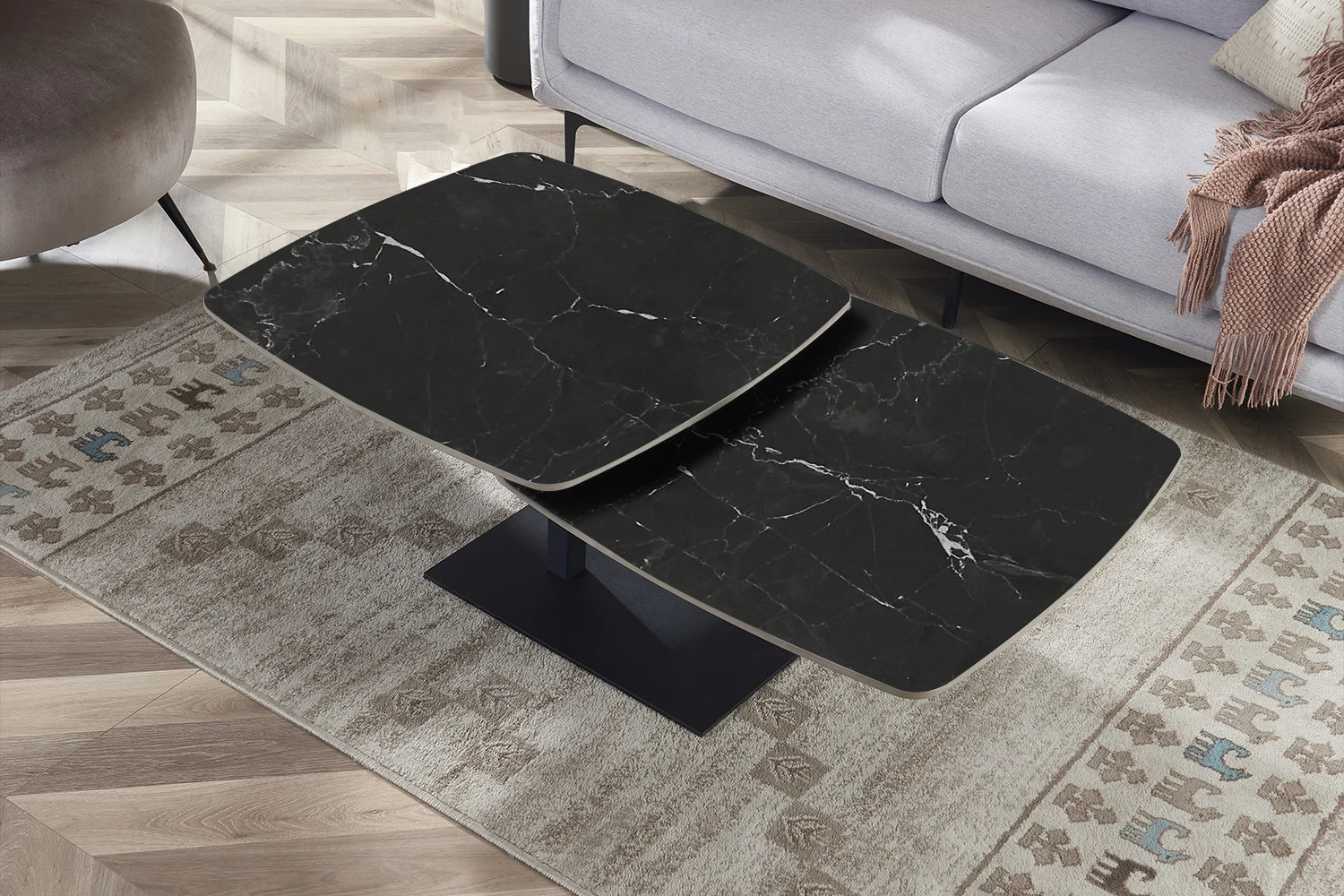 Een moderne woonkamer met de Salontafel Zwart Rond Steen, een zwarte salontafel met een marmeren blad, geplaatst op een gedessineerd tapijt en gecombineerd met een lichtgrijze bank en kussens op de achtergrond.