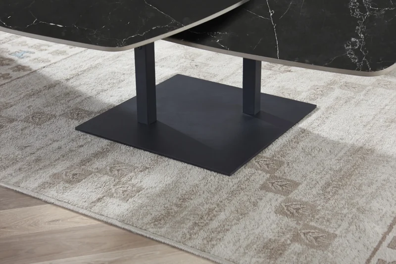 Een close-up van de Salontafel Zwart Rond Steen, een moderne zwarte ronde stenen salontafel, staand op een beige gedessineerd tapijt op een houten vloer.