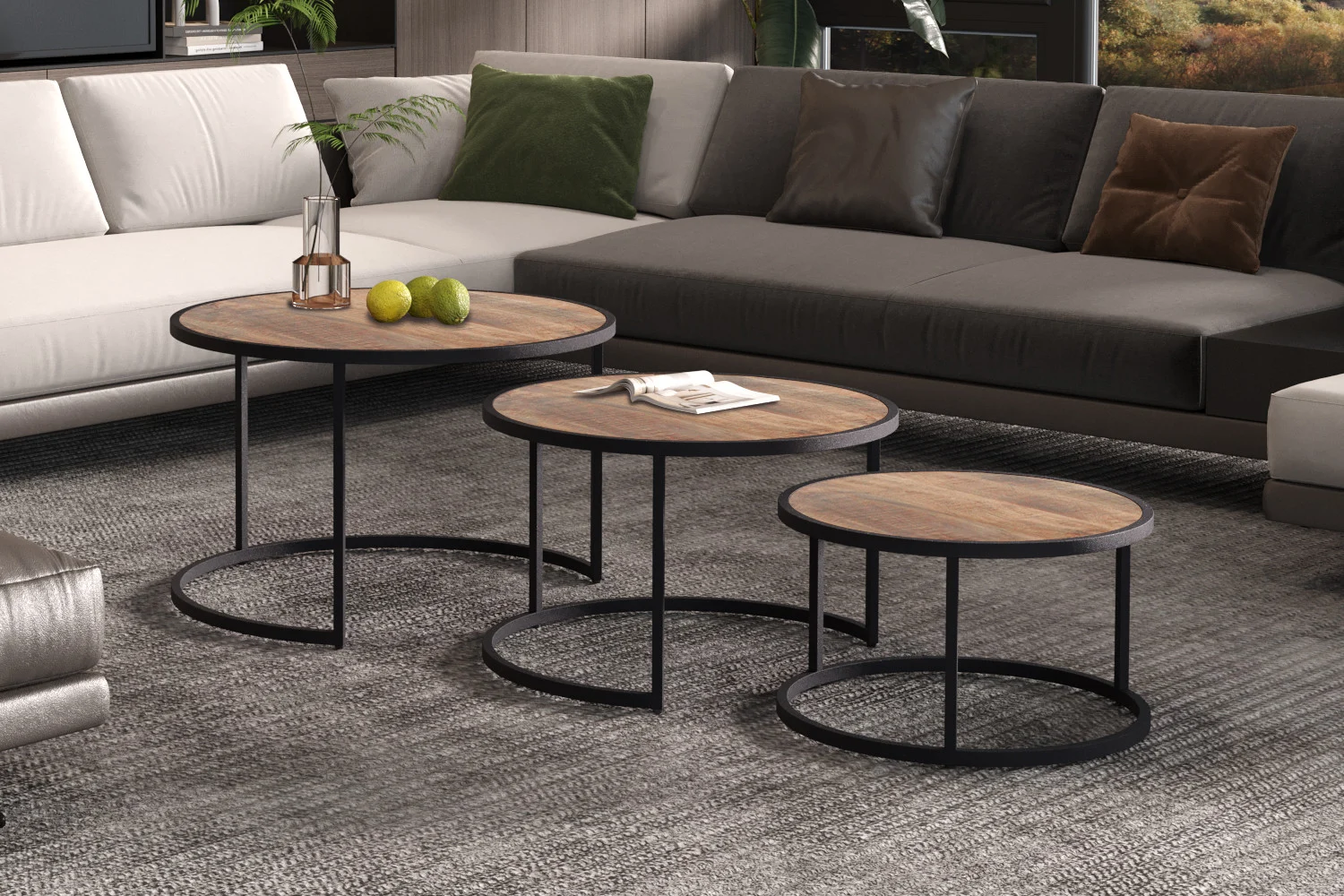 De Salontafel Mangohout Klassiek, met drie ronde houten tafels met een zwart metalen onderstel, staat voor een moderne sofa met neutrale kussens in een eigentijdse woonkamer. Een vaas, appels en een boek versieren de tafels.