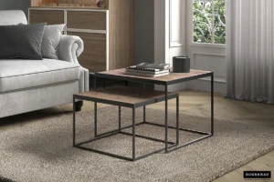Moderne woonkamer met de Salontafel Mangohout Modern Design: twee geneste houten tafels met zwarte metalen frames op een beige vloerkleed naast een grijze bank, boeken en een zwart kopje op de grotere tafel, met een groot raam en sierlijk ijzerwerk erachter.
