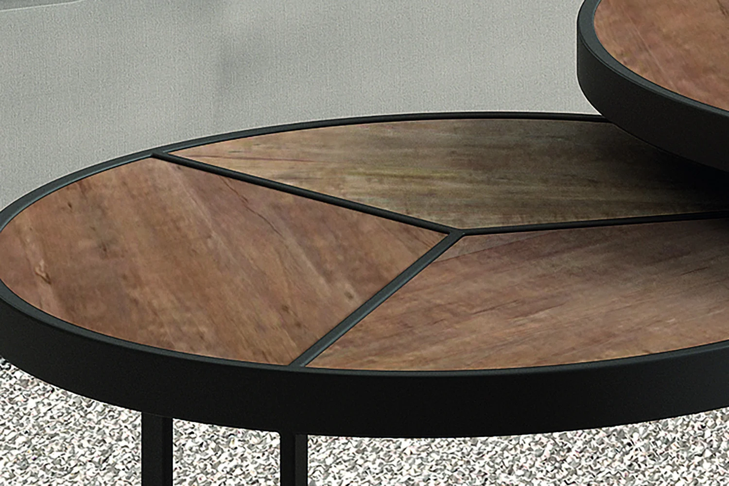 Close-up van Salontafel Mangohout Compact: twee ronde nesttafels met zwart metalen onderstel en geometrisch mangohouten inlegblad in een natuurlijk bruine afwerking tegen een grijs gestructureerd oppervlak.
