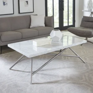 Een moderne woonkamer met een grijze bank, witte kussens en een Salontafel Rvs; op de tafel staan een geometrische vaas en een boek, terwijl grote ramen de ruimte vullen met natuurlijk licht.