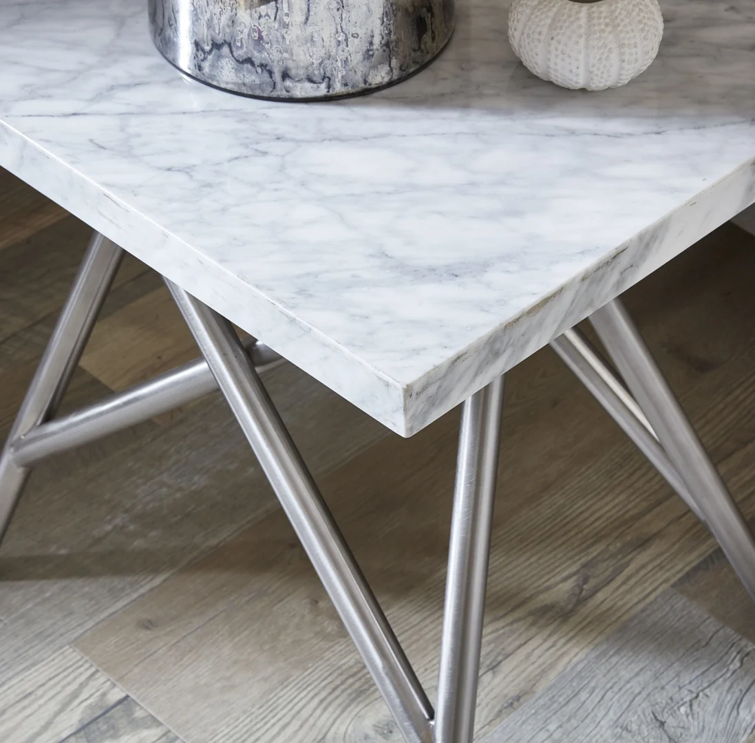 Een close-up van de Salontafel Rvs, met een marmeren blad en zilvermetallic onderstel op een houten vloer. Op de tafel staat een zilveren decorstuk en een kleine witte bol met structuur.