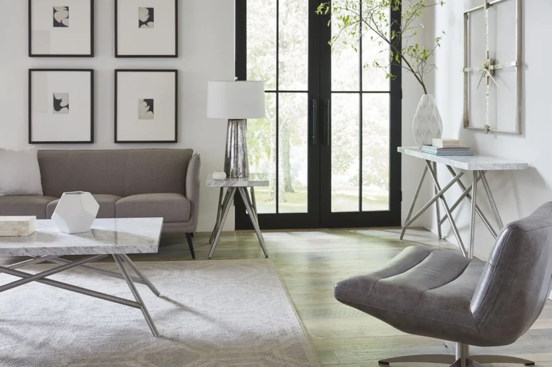 Moderne woonkamer met grijze meubels, een Koraal bijzettafel in marmer, abstracte muurkunst, een groot raam met zwarte kozijnen, lichte houten vloeren en een decoratieve plant op een consoletafel.