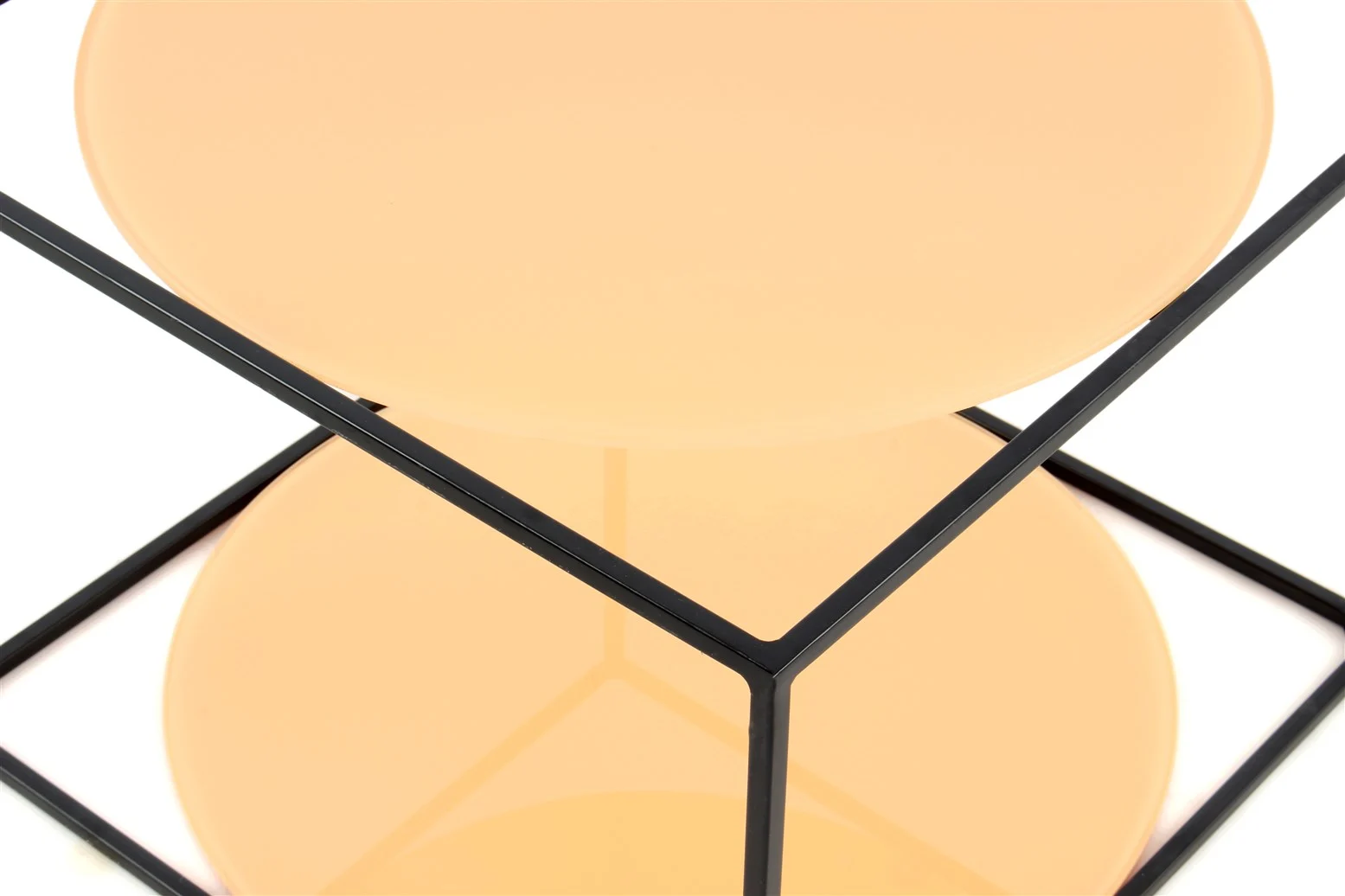 De Bijzettafel Oranje, Zwart Rond Ijzer heeft een perzikkleurig rond blad omlijst door zwart metaal, dat een kubusachtige vorm vormt. Het ronde oppervlak wordt weerspiegeld in een glanzende basis eronder.