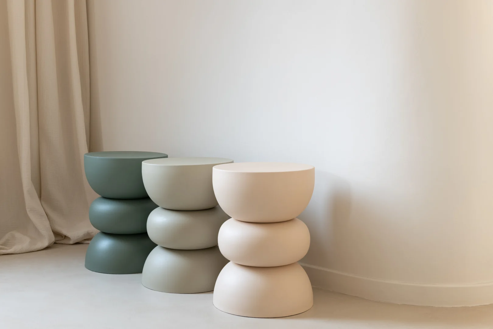 De Bijzettafel Lise IJzer Groen, een moderne bijzettafel in gedempt groen, staat bij een effen witte muur met een licht gordijn aan de linkerkant en voegt een minimalistisch en rustig accent toe aan de ruimte.